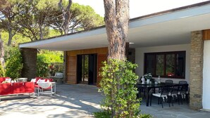 A covered outdoor patio with stone flooring, red outdoor furniture, and a dining area with black chairs and a table.