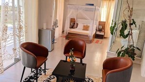 A hotel room with a bed, two chairs, a small table, a desk, and a large window with curtains. - Hary's aparthotel (Toliara)