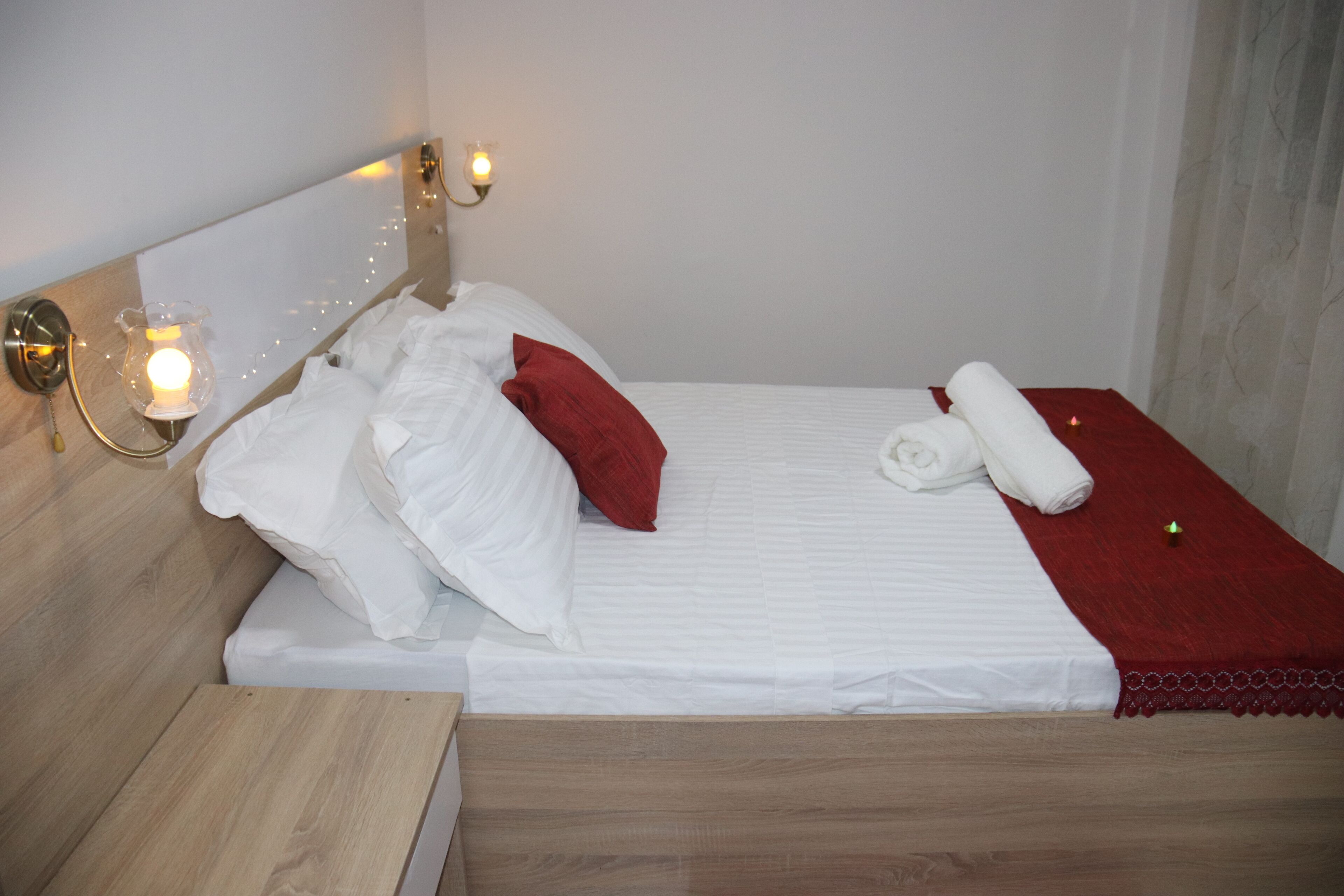 Un lit bien fait, avec une literie blanche et rouge, une tête de lit en bois et des lampes de chevet.