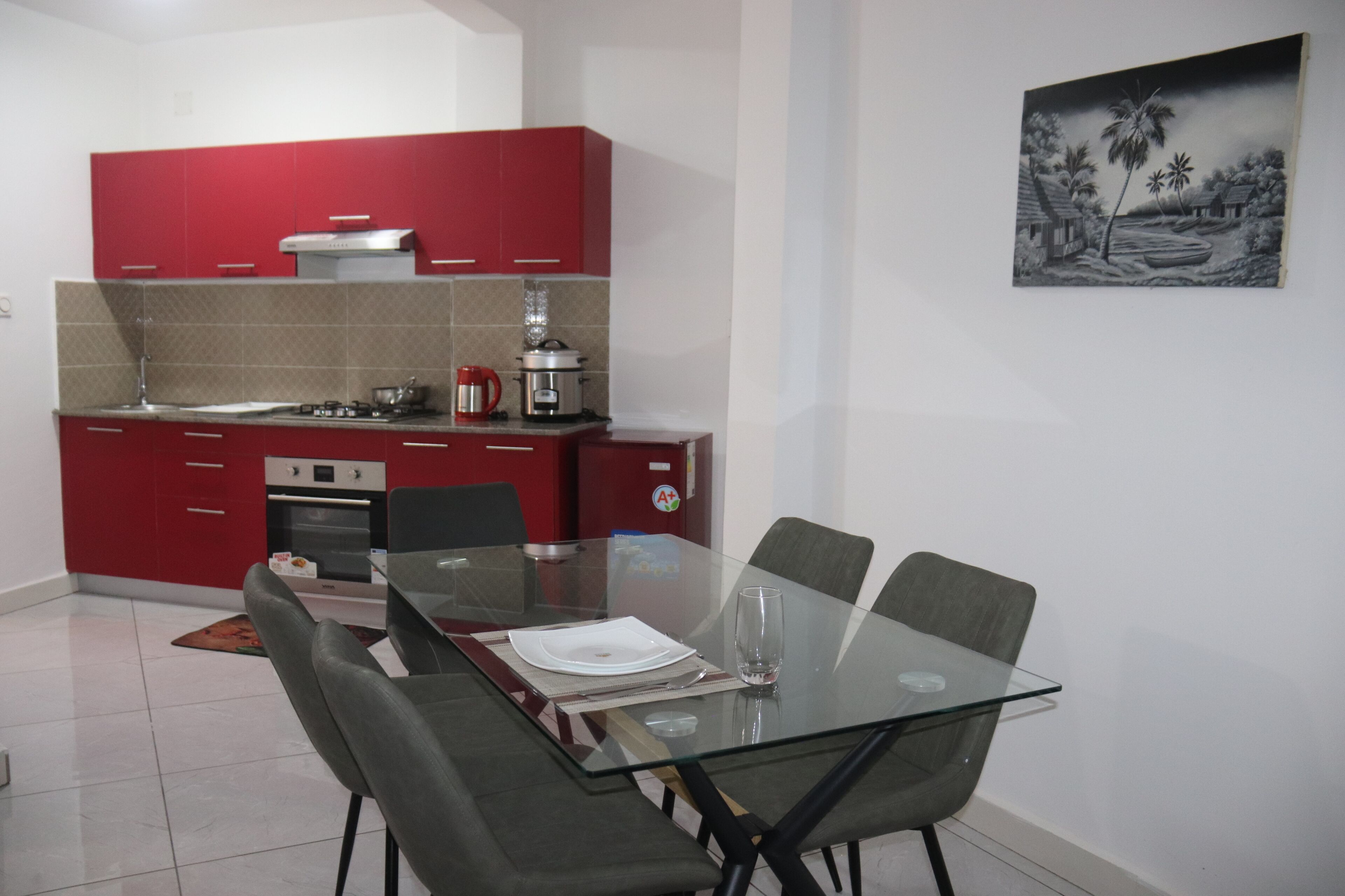 A modern kitchen with red cabinets, a glass dining table, and a painting on the wall.