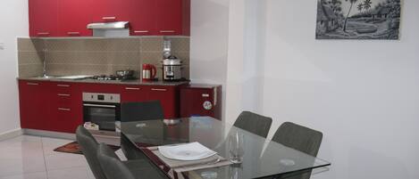 A modern kitchen with red cabinets, a glass dining table, and a painting on the wall.