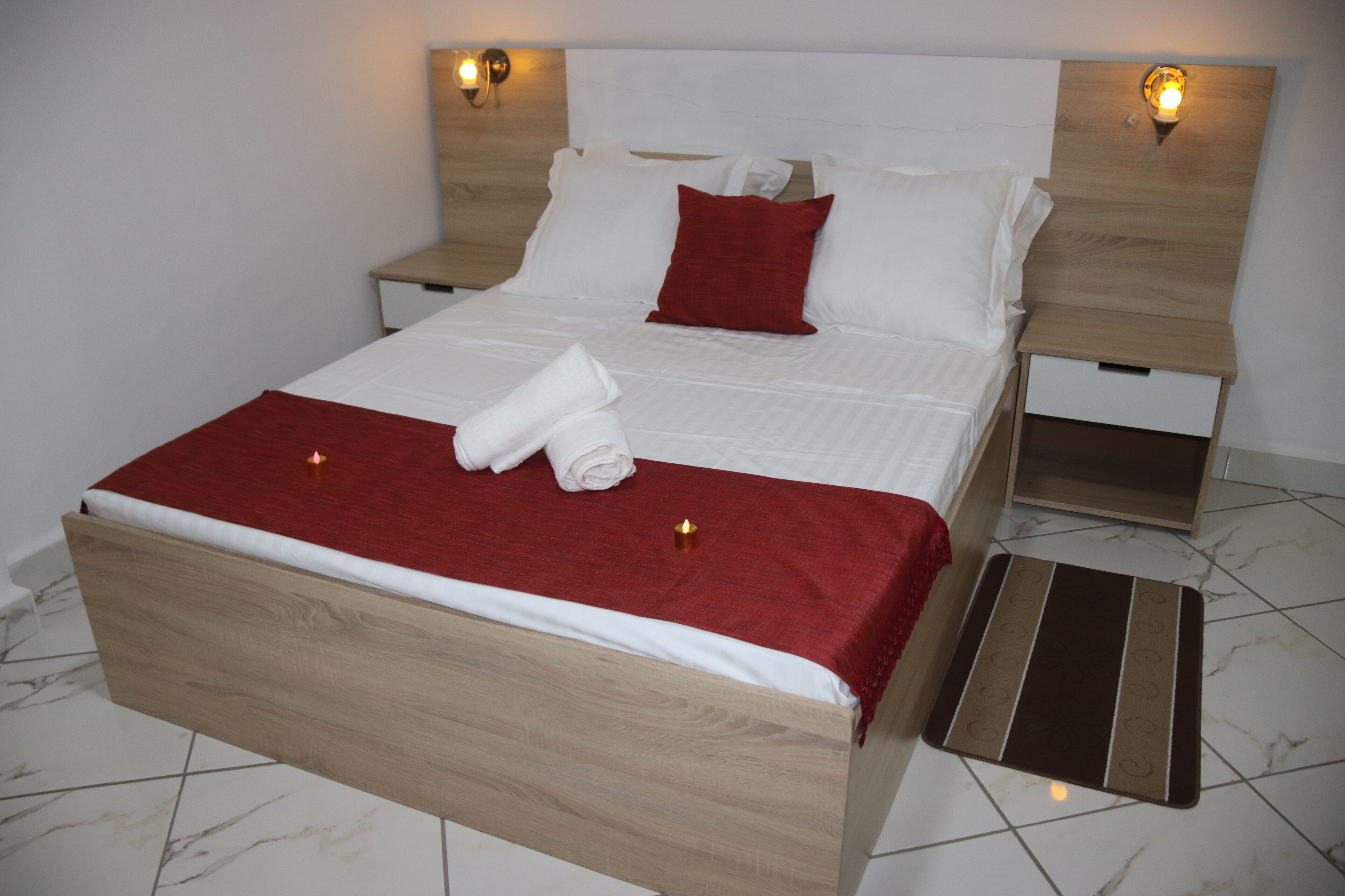 A neatly made bed with white and red bedding, wooden headboard, and bedside tables with lamps.
