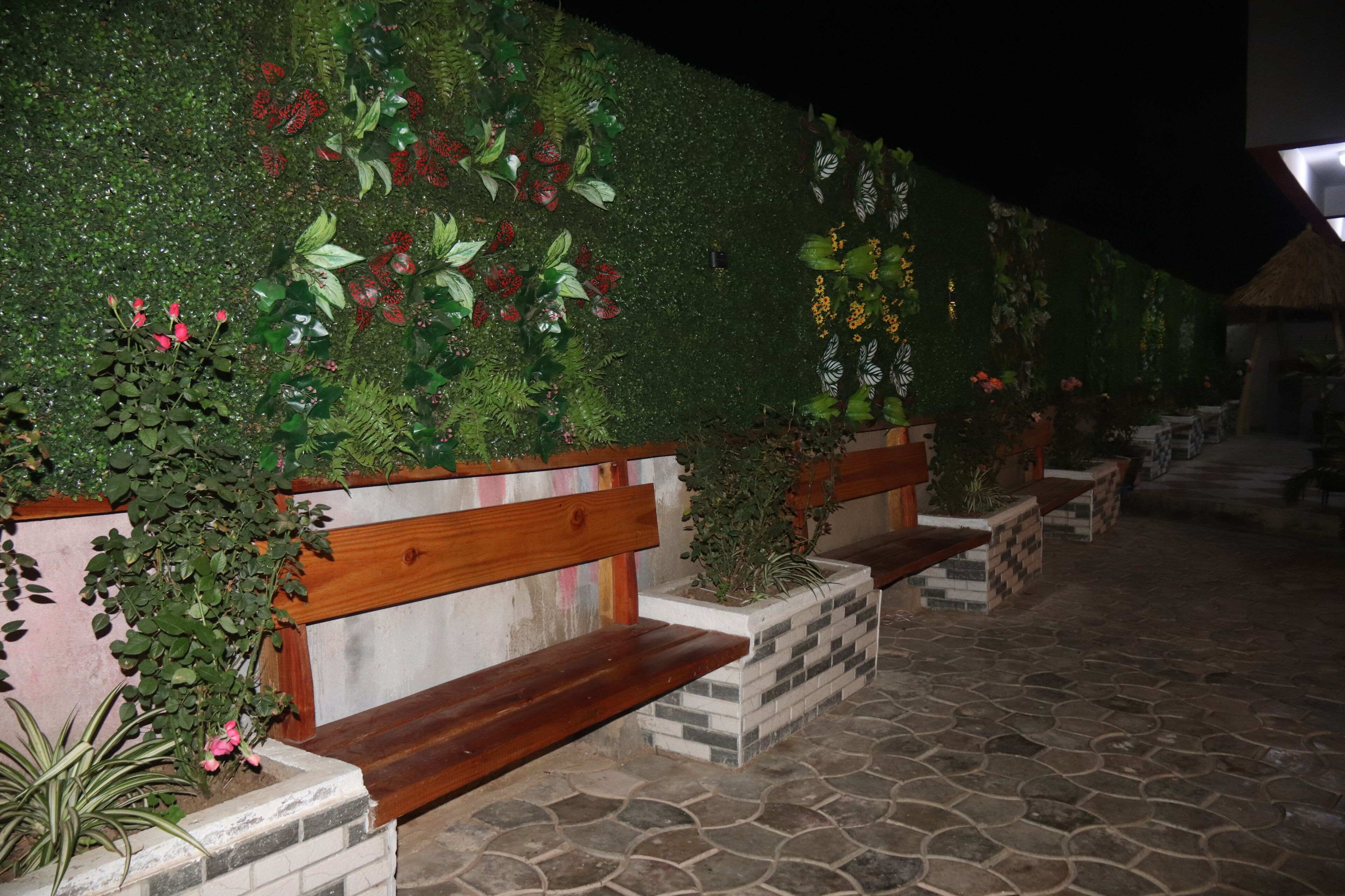 A stone-tiled patio with wooden benches and planters with various plants and flowers.