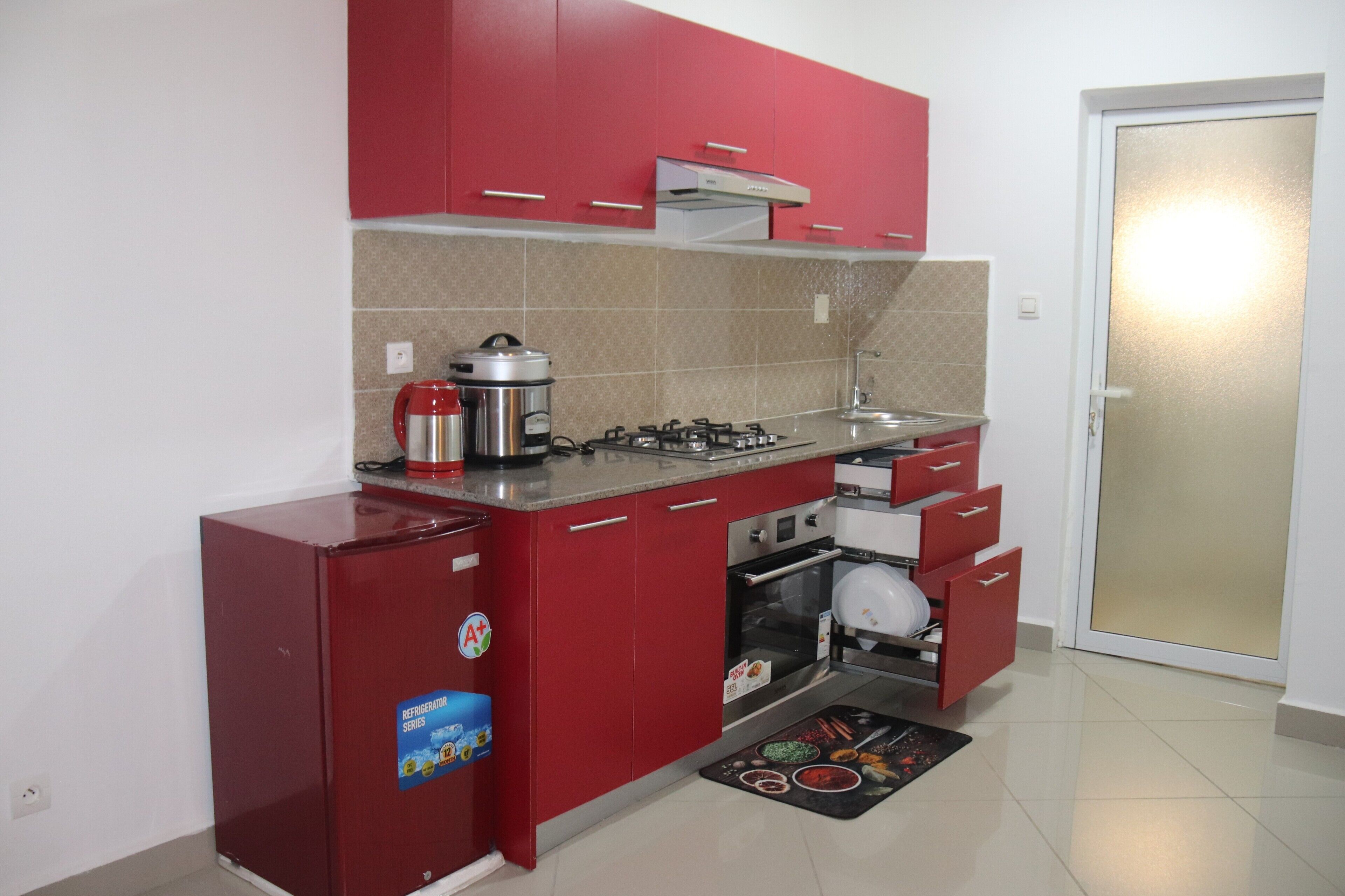 A compact kitchen with red cabinets, a built-in oven, a gas stove, and a refrigerator.