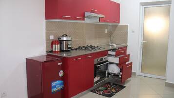 A compact kitchen with red cabinets, a built-in oven, a gas stove, and a refrigerator.