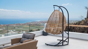 Una silla de mimbre y una hamaca colgante en un balcón con vistas al paisaje costero.