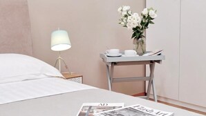 A neatly made bed with white linens, a bedside table with a lamp, a vase with white flowers, and two magazines on the bed. - ONEBEDROOM APARMENT (Roma)