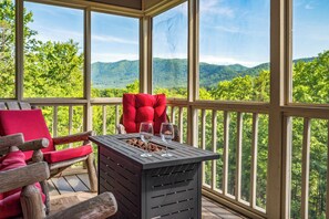 Ein überdachter Außenbereich mit Holzterrasse, einem rot gepolsterten Stuhl und einem Tisch mit zwei Gläsern Wasser.