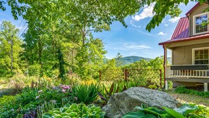 Ein Haus mit rotem Dach und einer Veranda, umgeben von üppiger Vegetation und einer Berglandschaft im Hintergrund.