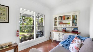 A cozy living room with a large window, a bookshelf, and a sofa. - Watta Cottage - Kangaroo Valley (Wattamolla)