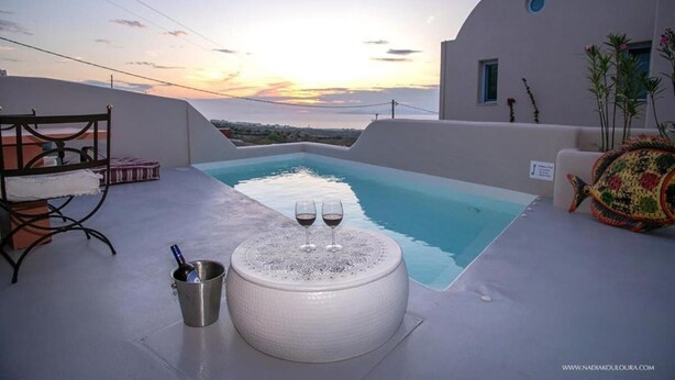 Un espace piscine aménagé sur le toit, avec une table ronde et deux verres de vin, offrant une vue sur le coucher du soleil.