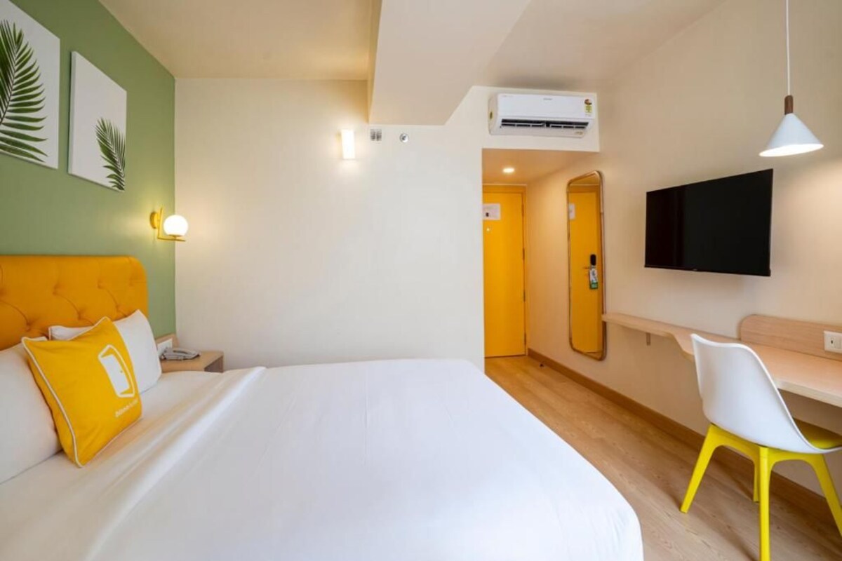 Een hotelkamer met een bed, een bureau, een stoel, een televisie en een airconditioning.