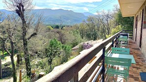 Ein Balkon mit Blick auf eine Berglandschaft, Holzgeländer und grüne Stühle.