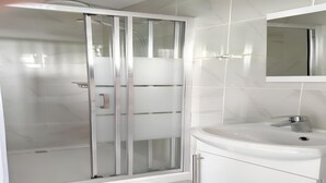 Ein modernes Badezimmer mit einer gläsernen Duschkabine, einem weißen Waschbecken und einem Spiegel darüber.