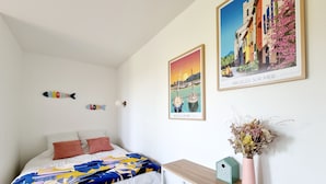 Une chambre à coucher avec un lit, une table de chevet ornée d’un vase et deux tableaux encadrés accrochés au mur.