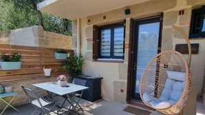 A patio with a table and chairs, a wicker chair, and potted plants. - Studio Terrasse « Louille » Vue sur le Parc Nature 5min Plages Argelès-sur-mer (Argeles-Sur-Mer)