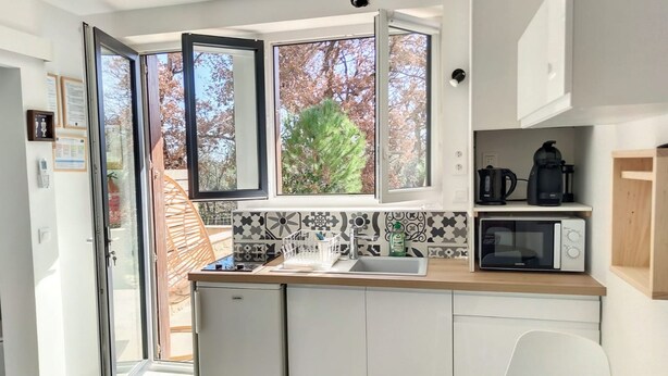 A modern kitchen with a large window, a microwave, a kettle, and a sink. - Studio Terrasse « Louille » Vue sur le Parc Nature 5min Plages Argelès-sur-mer (Argeles-Sur-Mer)
