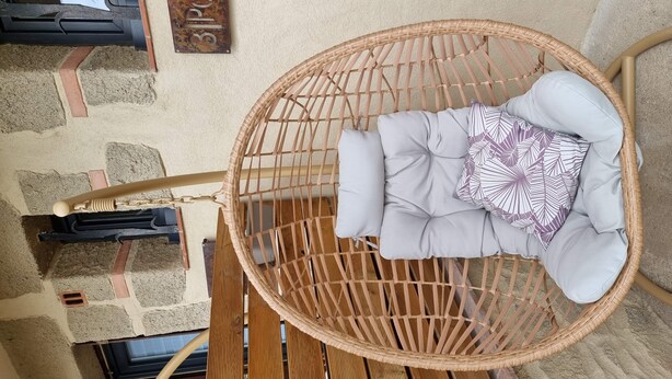 Une chaise en osier, agrémentée de coussins et d’un oreiller à motifs, adossée à un mur de pierre.