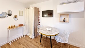 Une petite pièce moderne, dotée d’une table ronde en marbre, d’une chaise blanche, d’un téléviseur et d’un appareil de climatisation.