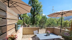 Une terrasse extérieure avec une table et des chaises, entourée de plantes en pot et de parasols.
