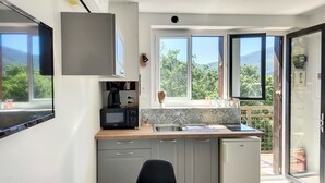 Una cocina moderna con armarios grises, un microondas integrado y una cafetera. Hay una ventana con vistas a zonas verdes y un balcón con puerta corredera.