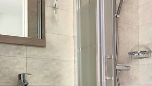 Un baño moderno con ducha envuelta en vidrio, lavamanos blanco y tocador de madera.