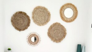Un dormitorio con una cama, dos almohadas, una mesita de noche con una planta y decoraciones circulares tejidas en la pared.