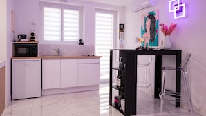 Una cocina moderna con armarios blancos, un microondas y una cafetera. Hay una mesa negra con un jarrón de flores y un cuadro en la pared.
