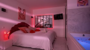 Un dormitorio con una cama grande, un televisor montado en la pared y un baño con bañera.