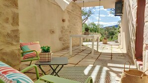 Un patio exterior acogedor con una mesa, sillas, una planta pequeña en maceta y un colgador de luz.