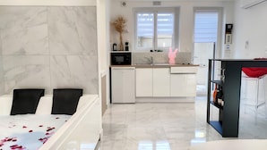 Una habitación de hotel moderna con baño de mármol, kitchenette y zona de comedor.