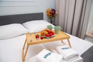 Enjoy a comfortable stay in a beautifully appointed room with a made bed, a tray with breakfast treats, and a vase with fresh flowers.