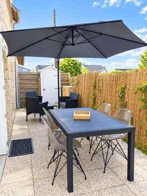 Een terras buiten met een tafel, stoelen, een grote parasol en een houten omheining.