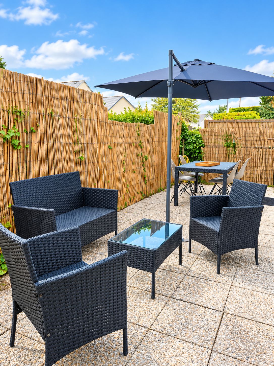 Eine Terrasse mit Korbmöbeln, einem Glastisch und einem großen Sonnenschirm.
