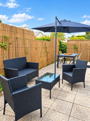 A patio area with wicker furniture, a glass table, and a large umbrella.