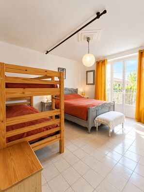 Een slaapkamer met een stapelbed, een enkel bed, een nachtkastje, een lamp en een raam met gordijnen.