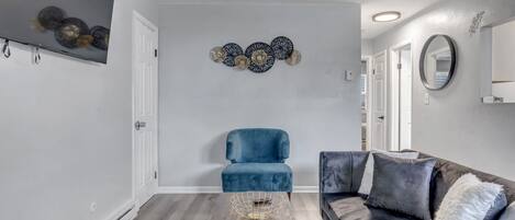 Una sala de estar moderna con un sillón azul, un sofá gris oscuro y una mesa de centro de madera.