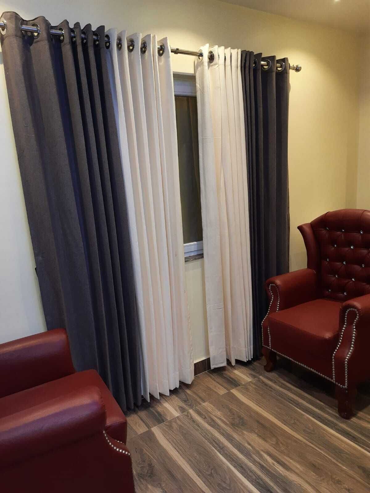 A room with a wooden floor, a red leather chair, and a window with curtains.