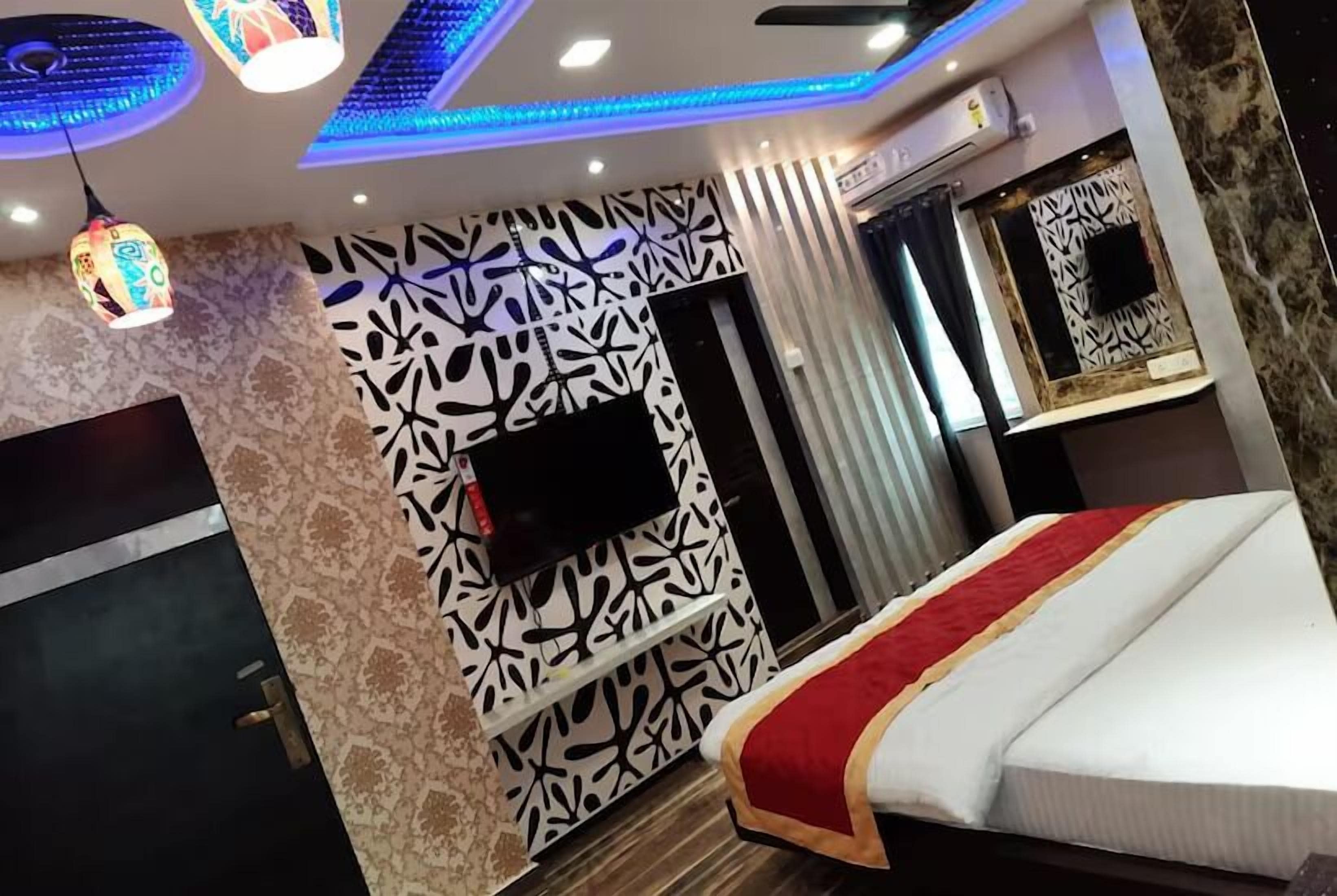 A modern hotel room with a patterned wall, a flat-screen TV, a bed with a red and white bedspread, and a ceiling fan.