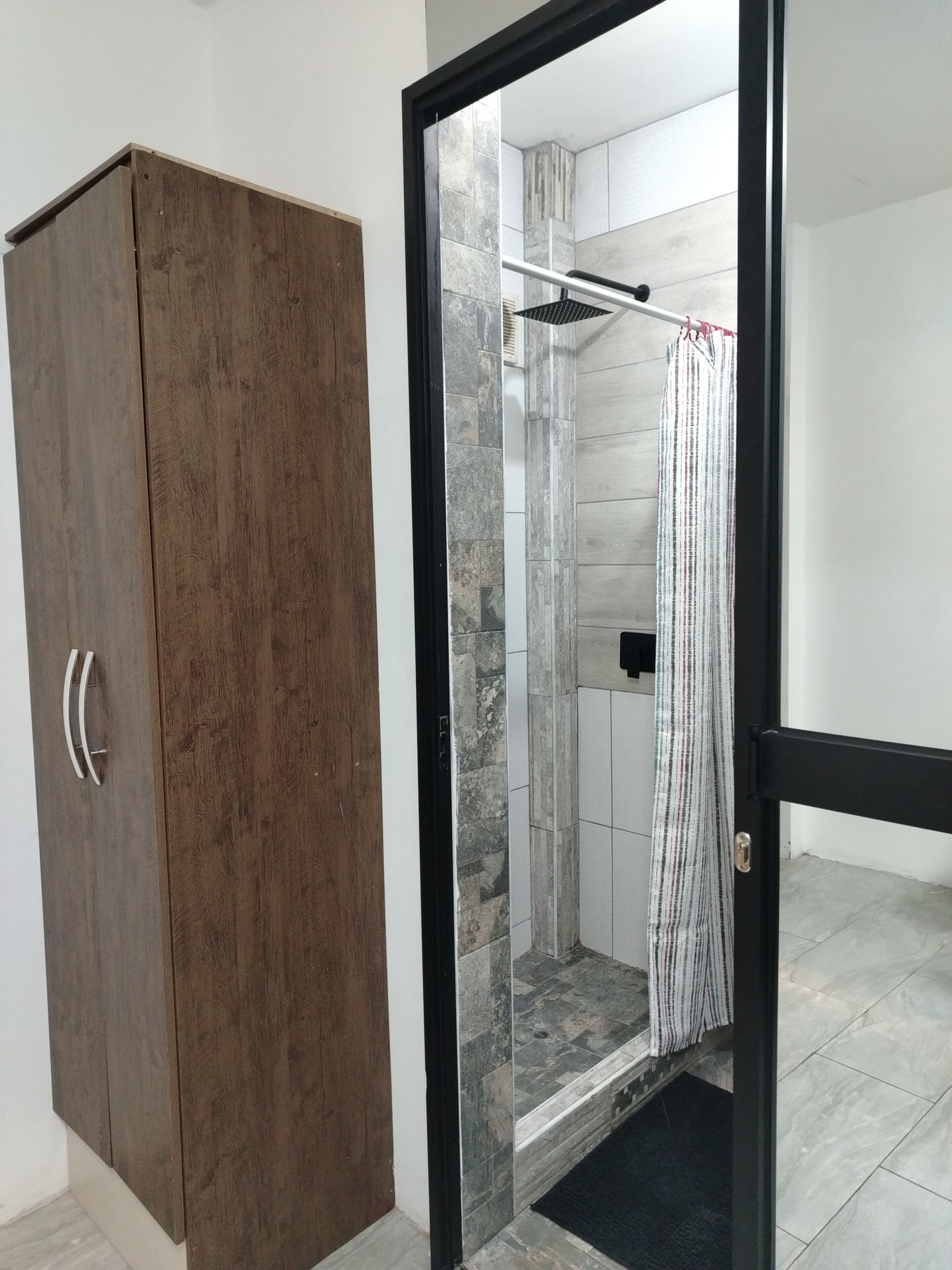 Une pièce avec une armoire en bois, un espace douche doté d’un rideau à rayures et un sol carrelé.