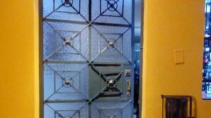 A door with a geometric pattern, a number plate above it, and a small light fixture to the right. - Chakana Family Home (Callao)