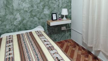 Une chambre à coucher avec un lit, une table de chevet, une lampe et un rideau.