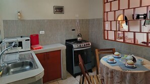 A compact kitchen with a gas stove, microwave, and sink. There's a dining table with a tablecloth and tea set. - Chakana Family Home (Callao)