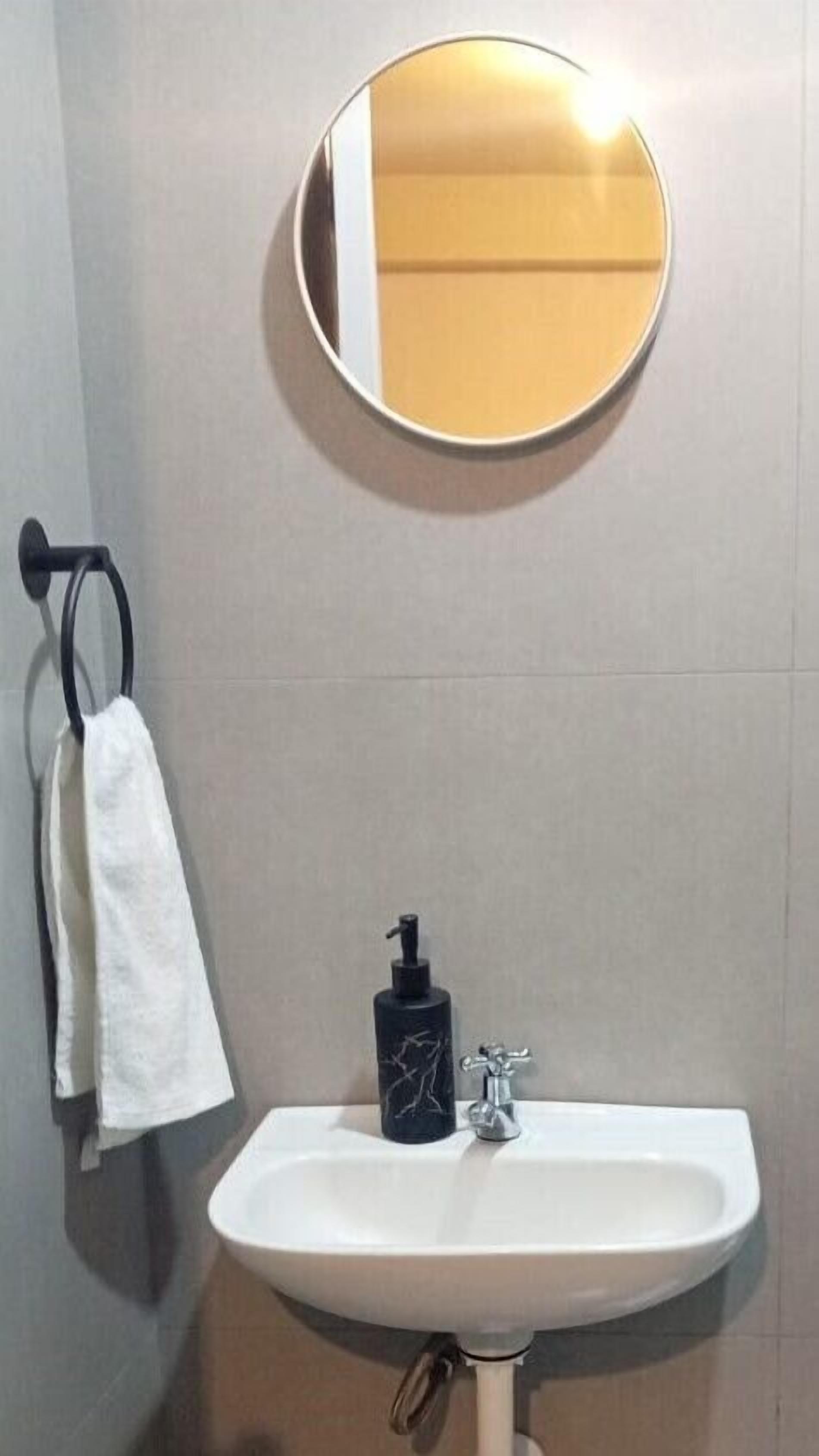 A bathroom with a round mirror, a white sink, and a black soap dispenser.