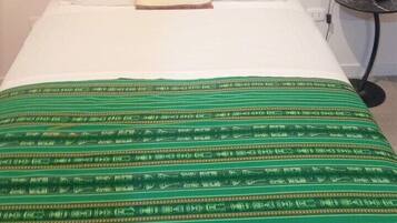 Una cama con cabecera oscura, almohadas blancas y colcha estampada verde.