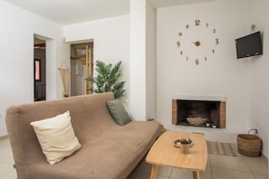 A living room with a sofa, a small table, a fireplace, and a wall clock. - Villa Selene in Gennadi (Γεννάδι)