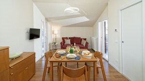 Un coin repas avec une table dressée pour quatre personnes, un téléviseur fixé au mur, un canapé rouge en arrière-plan et un meuble en bois sur la gauche.