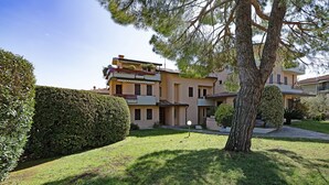 Un immeuble résidentiel avec une pelouse bien entretenue, un grand arbre et un ciel dégagé.