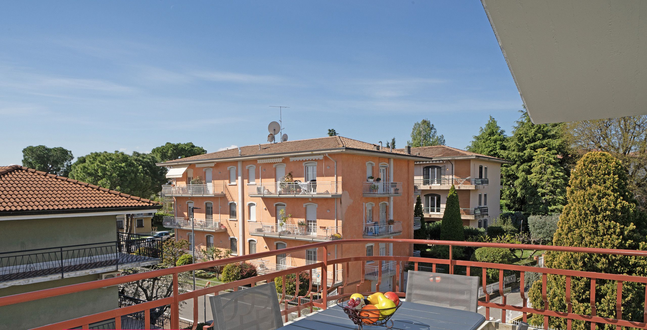 Een balkon met een tafel, stoelen en een schaal fruit.