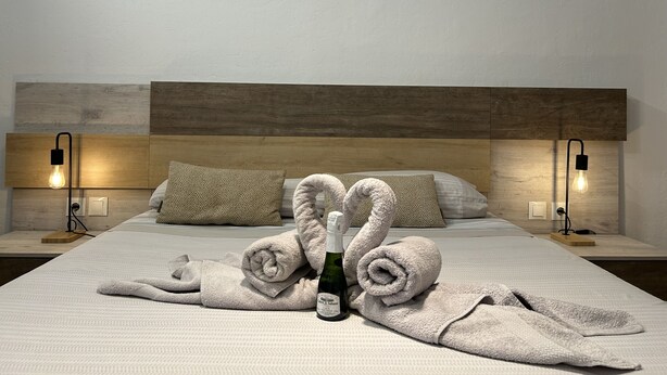 Una cama bien hecha con toallas, una botella de vino y dos lámparas en las mesitas de noche.